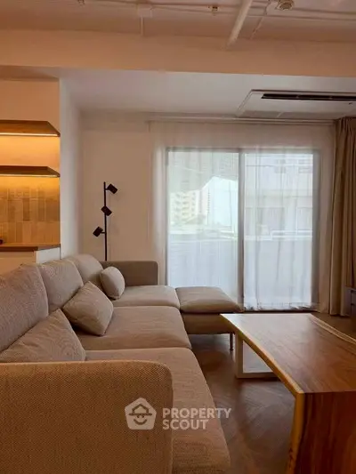Modern living room with cozy sectional sofa and wooden coffee table, featuring large window with sheer curtains.