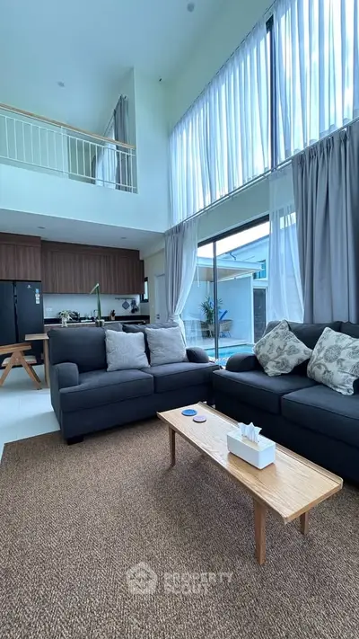 Spacious modern living room with high ceilings and large windows, featuring elegant furniture and natural light.