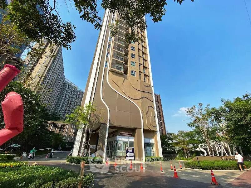 Modern high-rise building with unique facade design and lush greenery in urban setting.