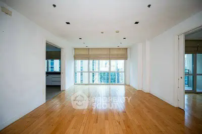 Spacious empty living room with hardwood floors and large windows offering city views.