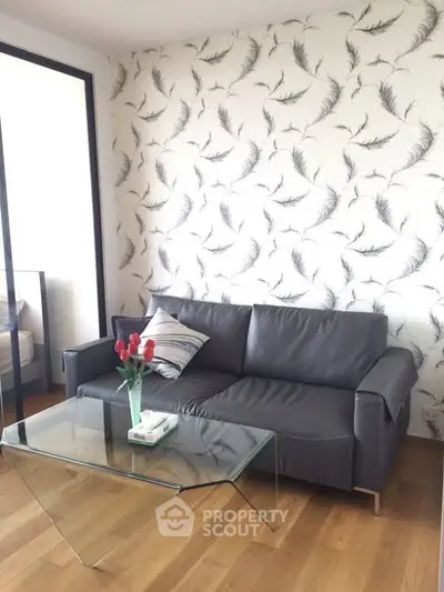 Stylish living room with modern sofa and glass coffee table, featuring elegant feather-patterned wallpaper.