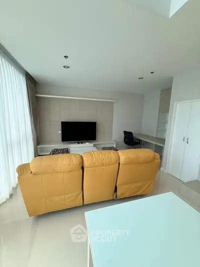 Spacious modern living room with large TV and comfortable seating in a bright apartment.