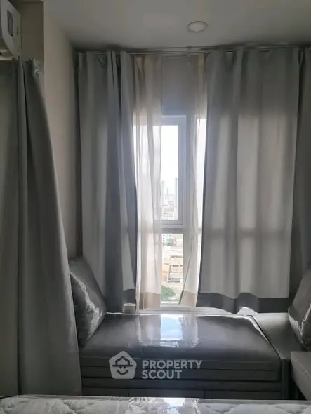 Cozy bedroom nook with city view through window, elegant curtains, and plush seating.