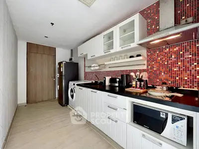 Modern kitchen with red mosaic backsplash, sleek cabinets, and appliances including washing machine and microwave.