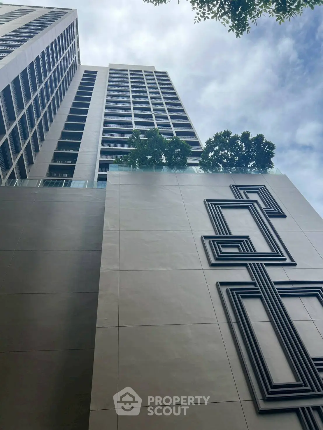 Modern high-rise building with unique geometric facade design and lush greenery.
