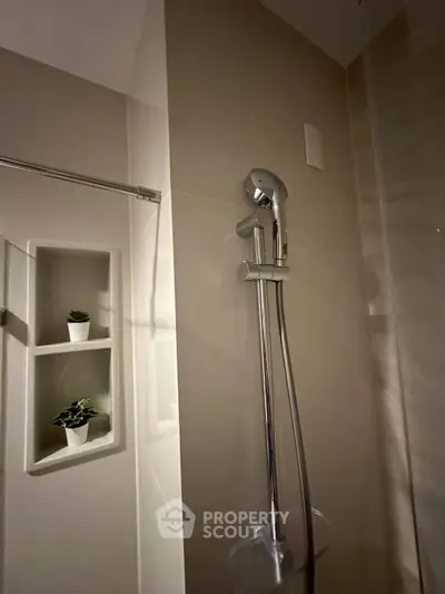 Modern bathroom with sleek showerhead and built-in shelf with plants, showcasing minimalist design.