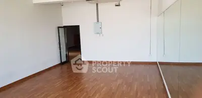Spacious empty room with wooden flooring and large mirror, ideal for dance or fitness studio.