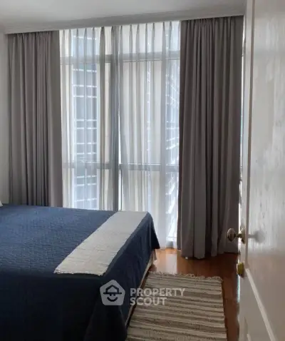 Spacious bedroom with large windows and elegant curtains in modern apartment.