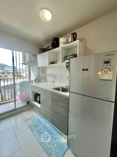Modern kitchen with sleek cabinets and stainless steel fridge, bright natural light from balcony.