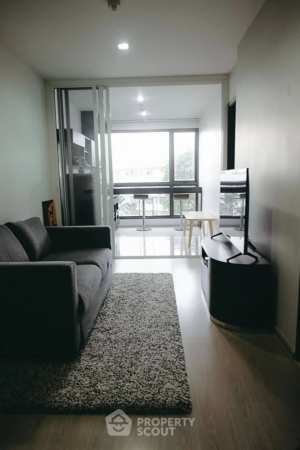 Modern living room with sleek sofa and large windows offering natural light and city views.