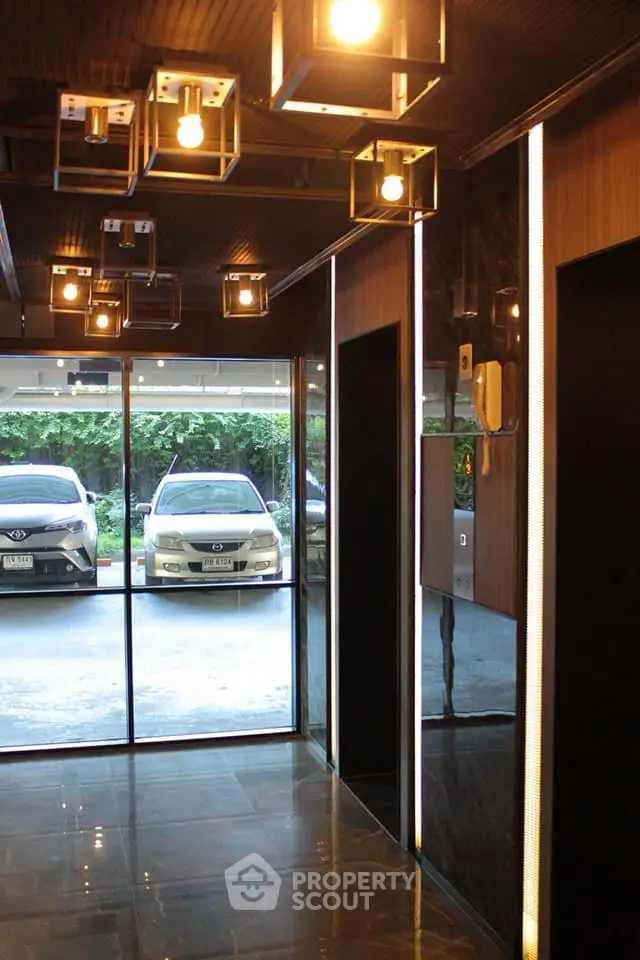 Modern building entrance with stylish lighting and parked cars outside.