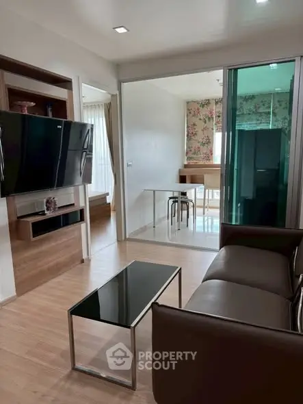 Modern living room with sleek furniture and open layout, featuring a wall-mounted TV and glass coffee table.