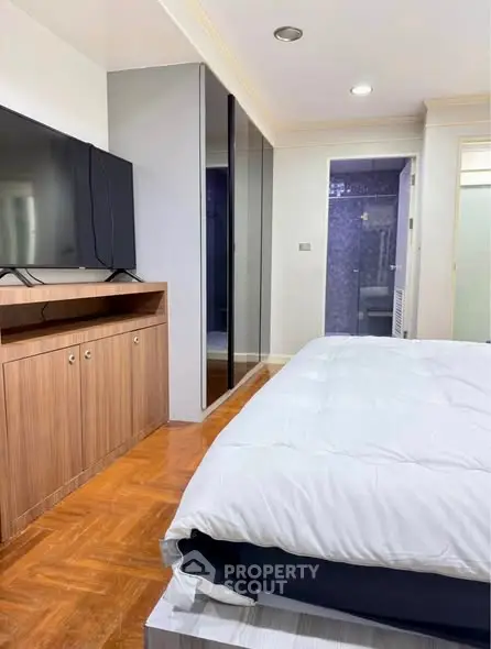 Spacious bedroom with modern decor and large TV, featuring sleek wooden flooring and ample storage space.