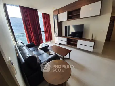 Modern living room with sleek furniture and large TV, featuring floor-to-ceiling windows and red curtains.