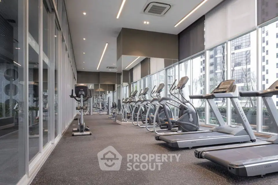 Modern gym with state-of-the-art equipment and floor-to-ceiling windows in luxury building.