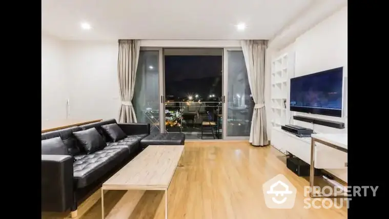 Spacious living room with polished hardwood floors, modern furniture, and large windows offering a stunning night view, perfect for urban living.