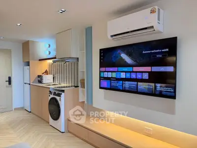 Modern living room with sleek kitchen, washing machine, and wall-mounted TV in stylish apartment.