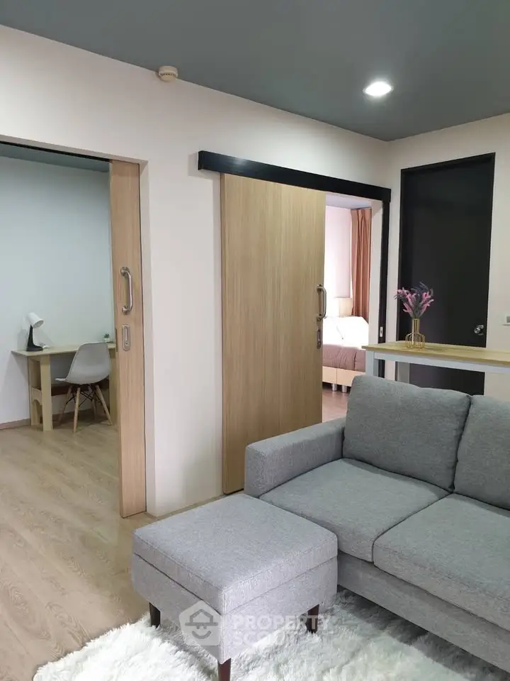 Modern living room with gray sofa and sliding doors leading to bedroom and study area.