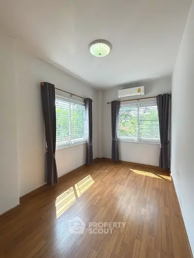 Bright empty bedroom with wooden flooring and large windows, perfect for customization.