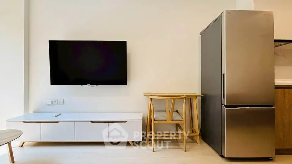 Modern living room with sleek TV, stylish furniture, and stainless steel fridge in a cozy apartment.