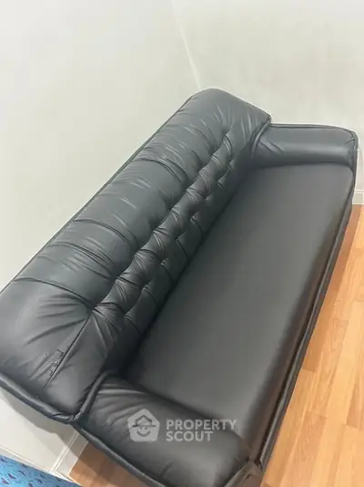 Sleek black leather sofa on wooden flooring in modern interior space.
