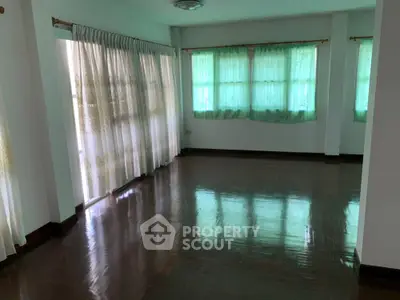 Spacious empty room with polished wooden floors and large windows with curtains