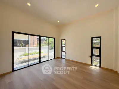 Spacious living room with large windows and garden view, featuring elegant wooden flooring and modern design.