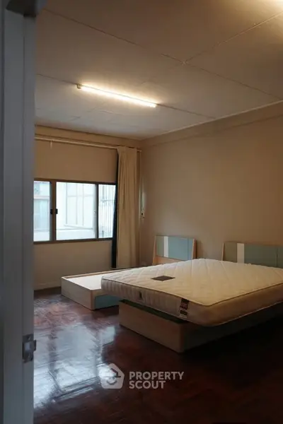 Spacious bedroom with wooden flooring and large window for natural light.