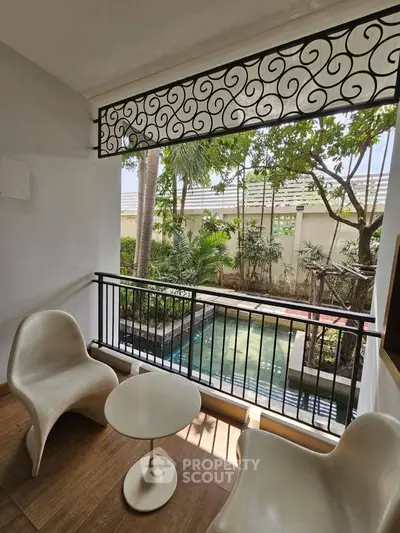 Charming balcony with stylish chairs overlooking a serene garden and pool view.