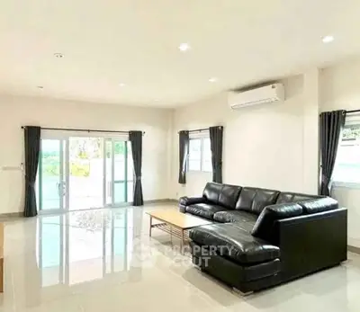 Spacious living room with modern black leather sofa and large windows for natural light.