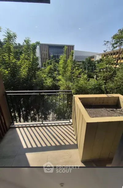 Charming balcony with lush green view and modern building backdrop, perfect for relaxation.