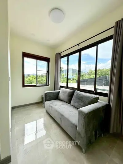 Bright living room with large windows and modern gray sofa, offering serene outdoor views.