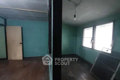 Spacious room with wooden floors and large windows in need of renovation.