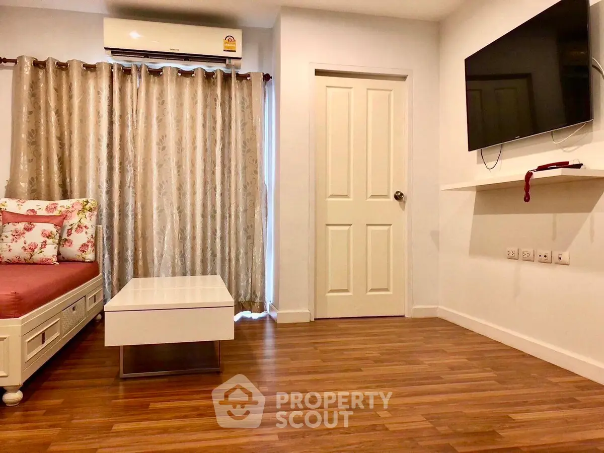 Cozy living room with wooden flooring, wall-mounted TV, and elegant curtains.