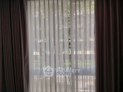 Elegant window with sheer curtains offering a glimpse of lush greenery outside, perfect for serene living.
