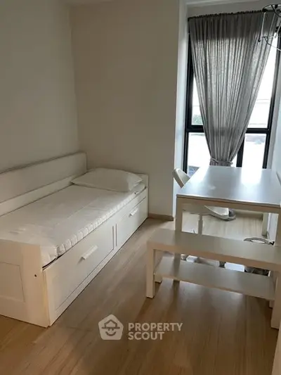 Cozy bedroom with single bed and study desk, natural light from large window.