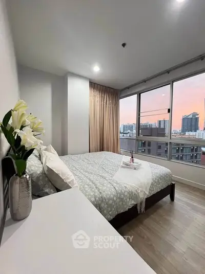 Modern bedroom with large windows offering stunning city views at sunset.