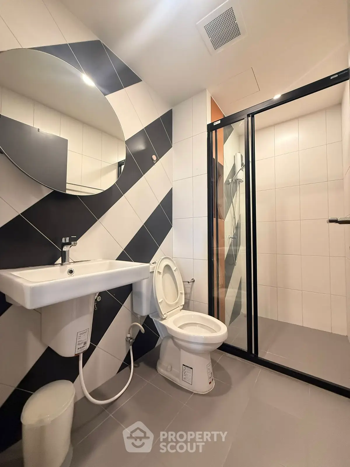 Modern bathroom with sleek design, featuring a round mirror, glass shower, and stylish tile patterns.