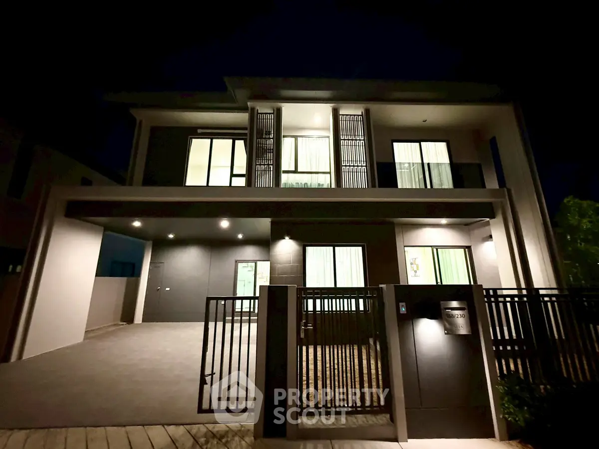 Modern two-story house exterior with sleek design and illuminated windows at night.