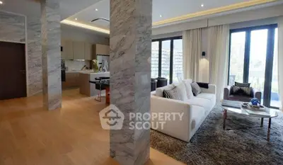 Luxurious open-plan living room with modern kitchen, marble accents, and large windows offering natural light.