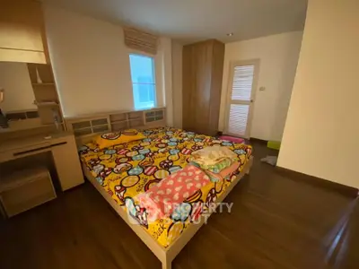 Cozy bedroom with colorful bedding and wooden flooring, featuring a built-in wardrobe and natural light.
