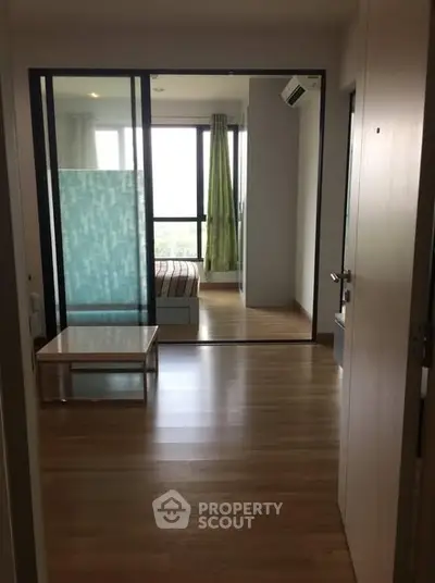 Modern apartment interior with wooden flooring and glass partition, featuring a cozy bedroom.