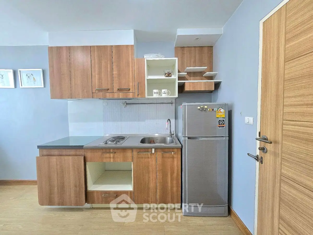 Modern compact kitchen with wooden cabinets and stainless steel fridge in cozy apartment.