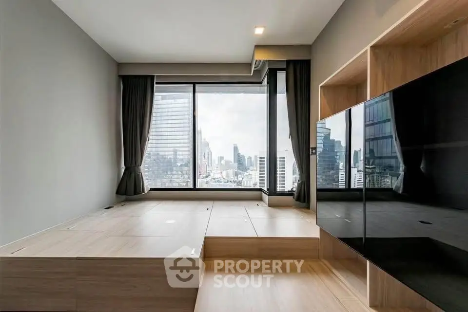 Modern living room with large window offering stunning city views, featuring sleek wooden flooring and built-in storage.