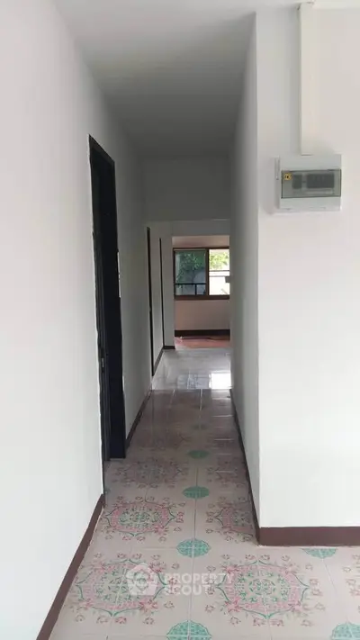 Bright hallway with patterned tiles leading to a spacious room with large windows.