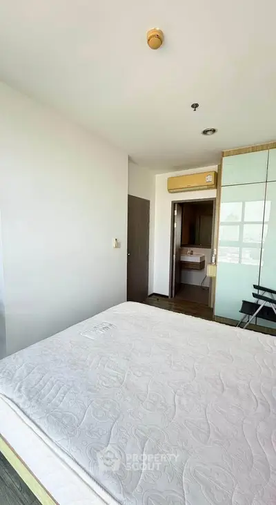 Spacious bedroom with large window and modern decor in a high-rise apartment.
