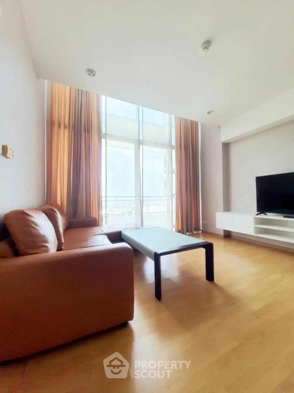 Spacious living room with high ceilings and large windows, featuring modern furniture and natural light.
