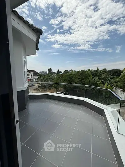 Spacious balcony with glass railing offering scenic views of lush greenery and clear skies.