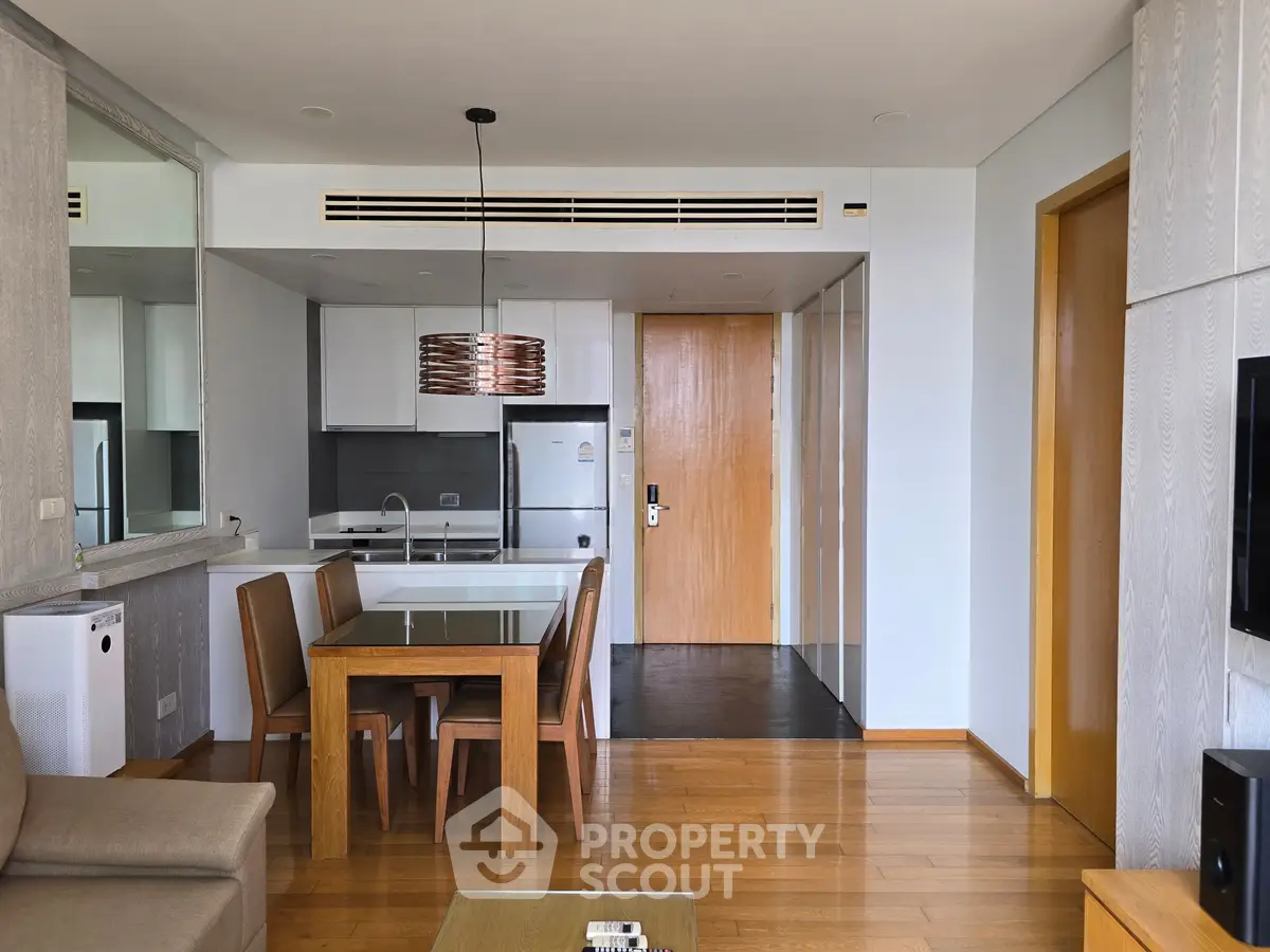Modern open-layout living room with sleek kitchen and dining area, featuring wooden flooring and contemporary furniture.