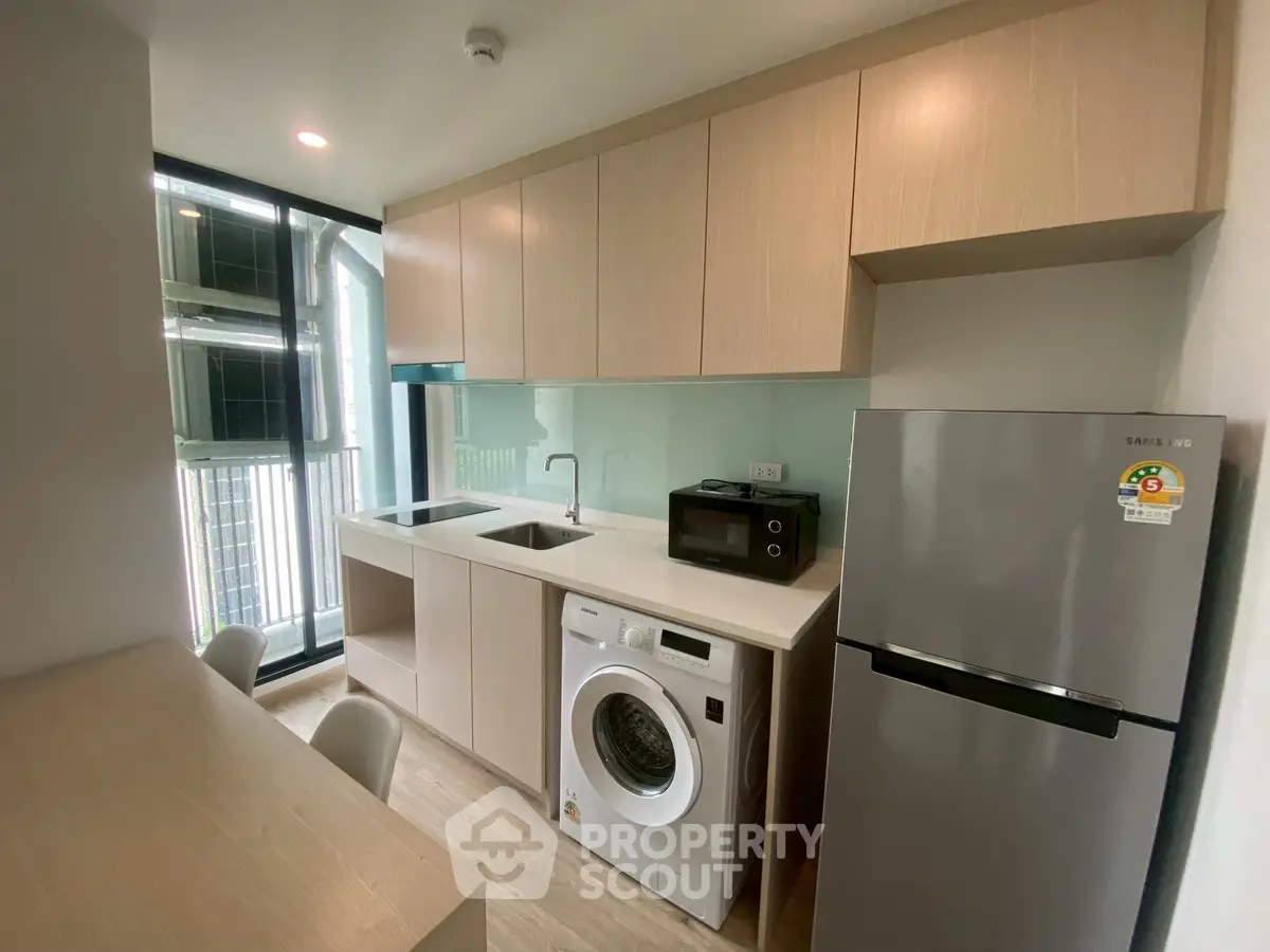 Modern kitchen with washing machine, fridge, and ample cabinetry in a sleek apartment.